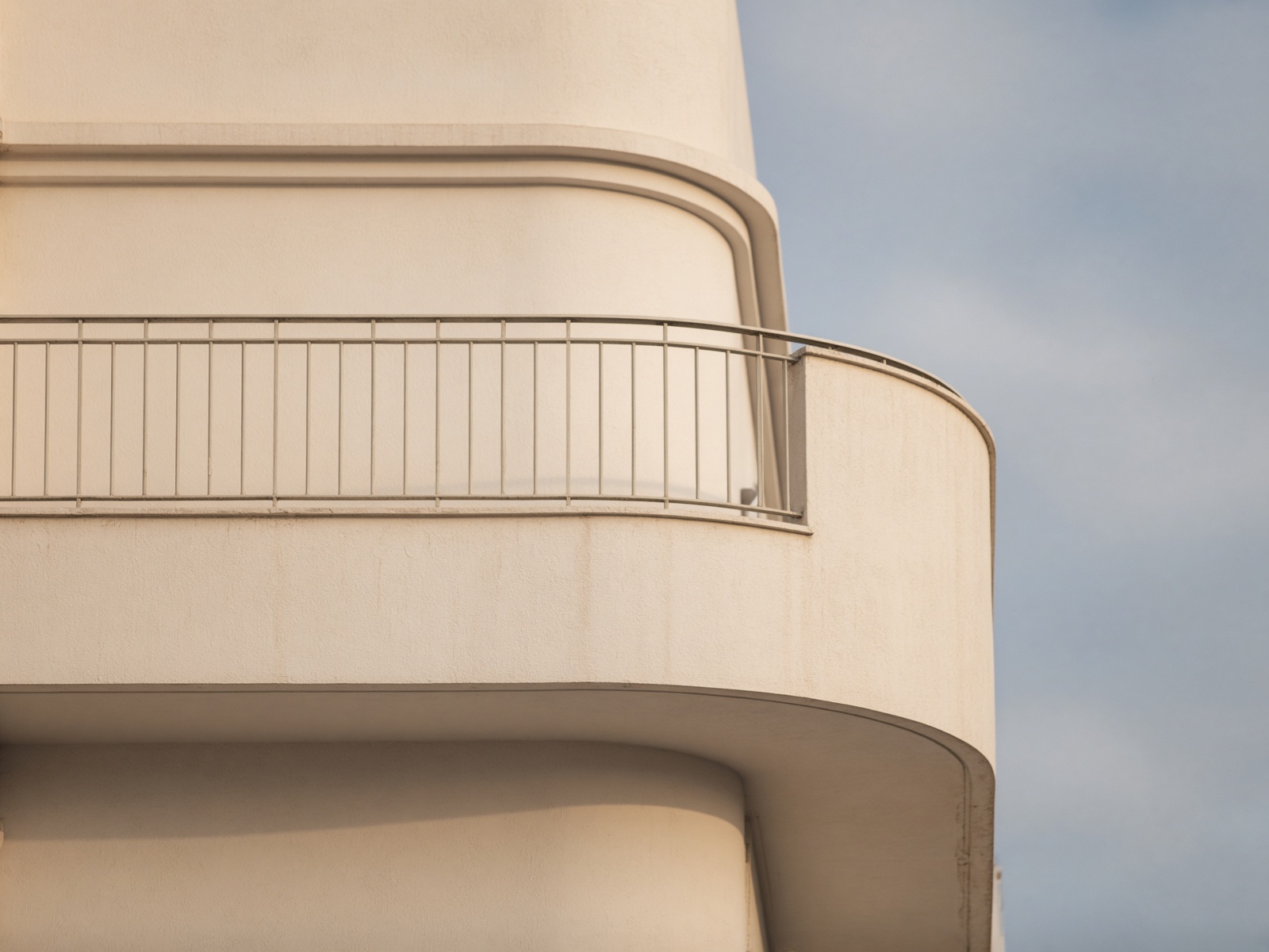 Sun-washed Bauhaus balcony: curved plaster and a simple metal railing against a pale sky.